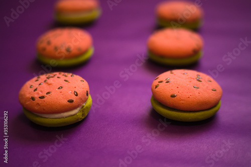 Multi-colored green and pink, bright cookies with two halves dressed with filling and sprinkled with sesame seeds on a bright purple color background.