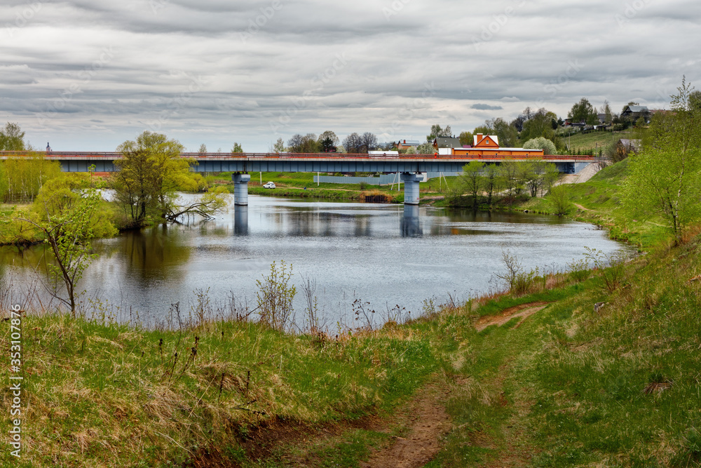 Fototapeta premium An automobile bridge over a small river surrounded by cottages and farm fields.