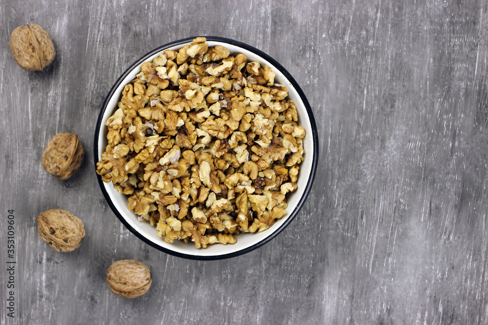 Walnut kernels in a bowl and whole nuts on an old gray table