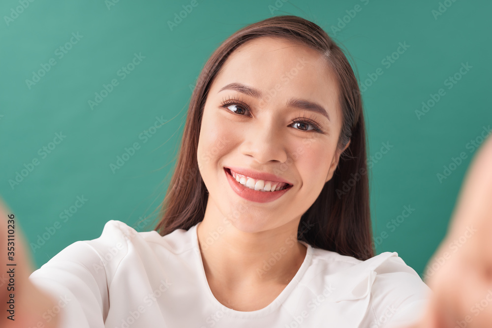 Fototapeta premium Portrait of a smiling young casual asian woman taking selfie isolated over green background