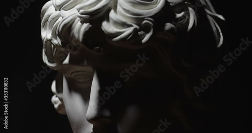 Epic studio close-up  shot of a gypsum head with moving and changing lighting. The play of light and shadow on half the face of a white statue of a man. On a black background isolated 4k