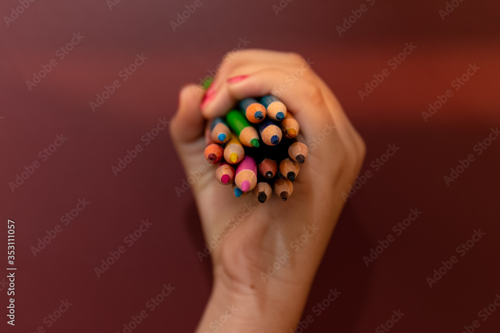 Crop view of hands holding multicolored pencils and painting brush with Maroon background to draw something. Crop view of hands holding multicolored pencils and painting brush with Maroon background to draw something.