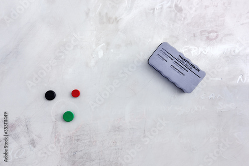 Magnetic eraser sponge and magnets hanging on dirty white board. Text on sponge is translated 
