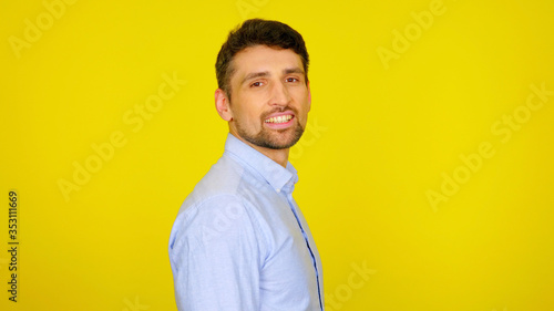 Handsome bearded man in a light blue shirt smiles. Businessman looking at the camera on a yellow background with place for text