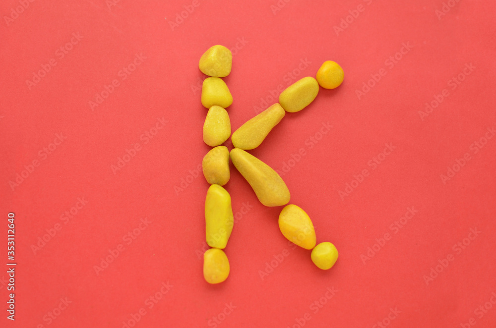 Letter K made of old Yellow pebbles on a red background Letter K made of old Yellow pebbles on a red background