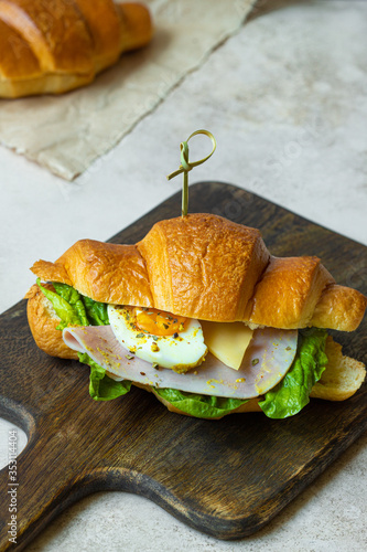 ham croissant sandwich with salad, cheese and egg on dark wooden board. close up