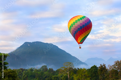 Colorful hot air balloon is flying over the mountain and jungle at sunrise