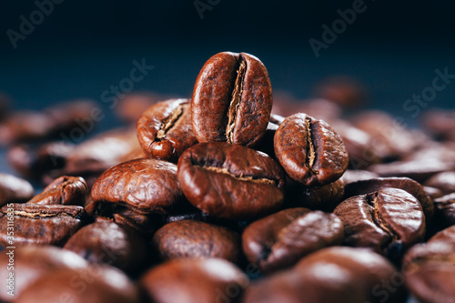 Grains of black coffee on a black granite countertop with yellow light from behind. Advertising photo of coffee. Pour coffee. Macro photo of grains..