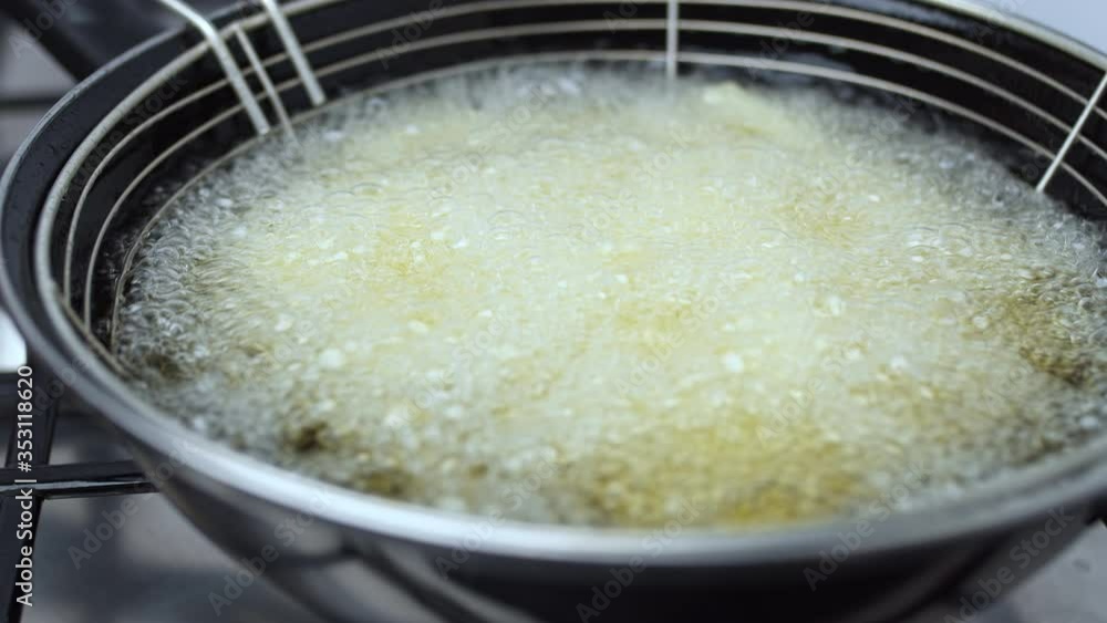 A close-up look of a lot of bubbles over the homemade french fries in the boiling oil in a basket in a pan on the gas stove. French fries becoming gold because of their cooking. A close-up look of a lot of bubbles over the homemade french fries in the boiling oil in a basket in a pan on the gas stove. French fries becoming gold because of their cooking.