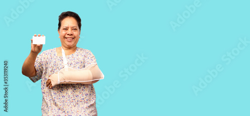 Elderly Asian woman broken arm cast  holding credit card on blue background in studio With copy space.