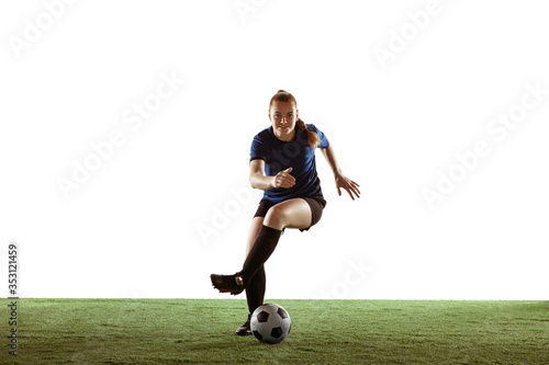 Young female soccer or football player with long hair in sportwear kicking ball for the goal, training on white studio background. Concept of healthy lifestyle, professional sport, motion, movement.