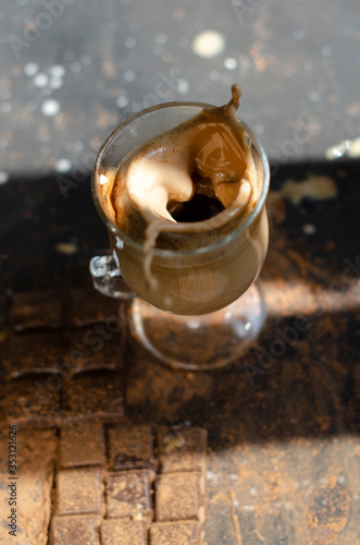 a glass of latte on a table with pieces of dark chocolate and cocoa