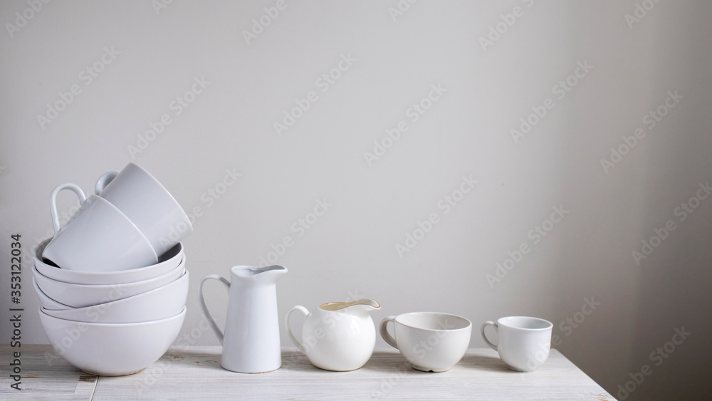 A set of white dishes on the table in the kitchen. Bowls, cups of various shapes, milk jugs, kitchen utensils for tea. A set of white dishes on the table in the kitchen. Bowls, cups of various shapes, milk jugs, kitchen utensils for tea.