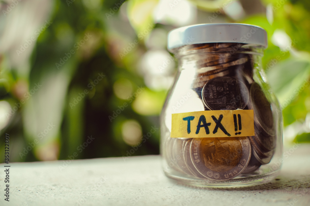 The glass jar full with the coins. TAX word on the glass jar. Financial and tax concept. Thai bath money in a jar. The glass jar full with the coins. TAX word on the glass jar. Financial and tax concept. Thai bath money in a jar.