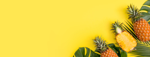 Beautiful pineapple on tropical palm monstera leaves isolated on bright pastel orange yellow background, top view, flat lay, overhead above summer fruit.