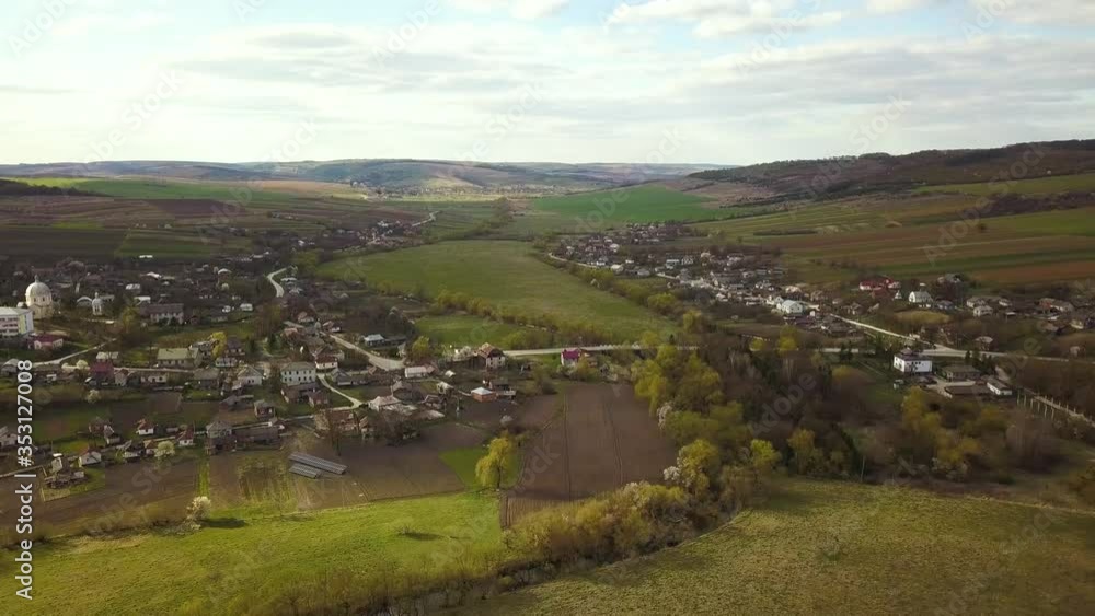 Aerial view of countryside village with small houses among green trees with farm fields and distant forest in summer. Aerial view of countryside village with small houses among green trees with farm fields and distant forest in summer.