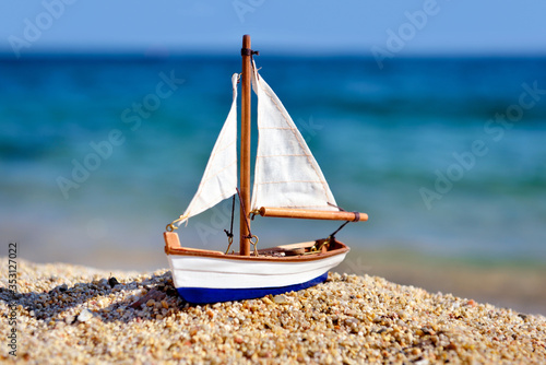 Photography Miniature toy sailboat on the beach against the background of the sea and waves