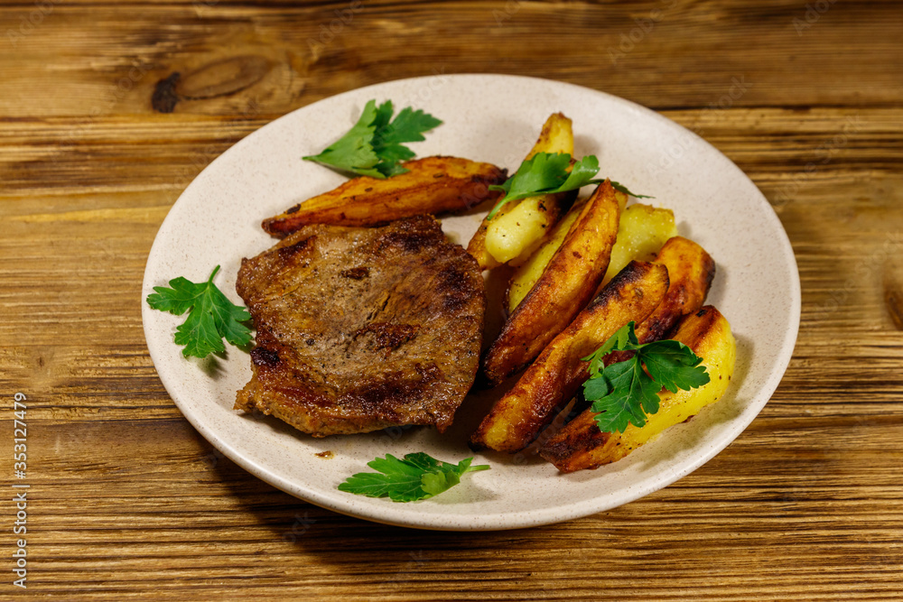 Fried beef steak with potato wedges on wooden table Fried beef steak with potato wedges on wooden table