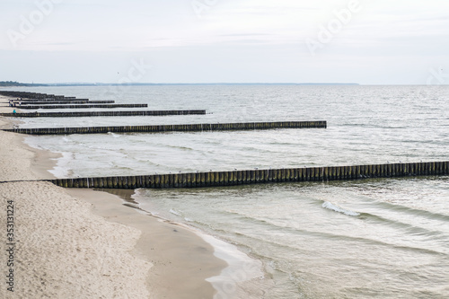 Breakwater on seashore from wooden logs. Seagulls are sitting on it in the middle of sea. Cloudy rainy weather.