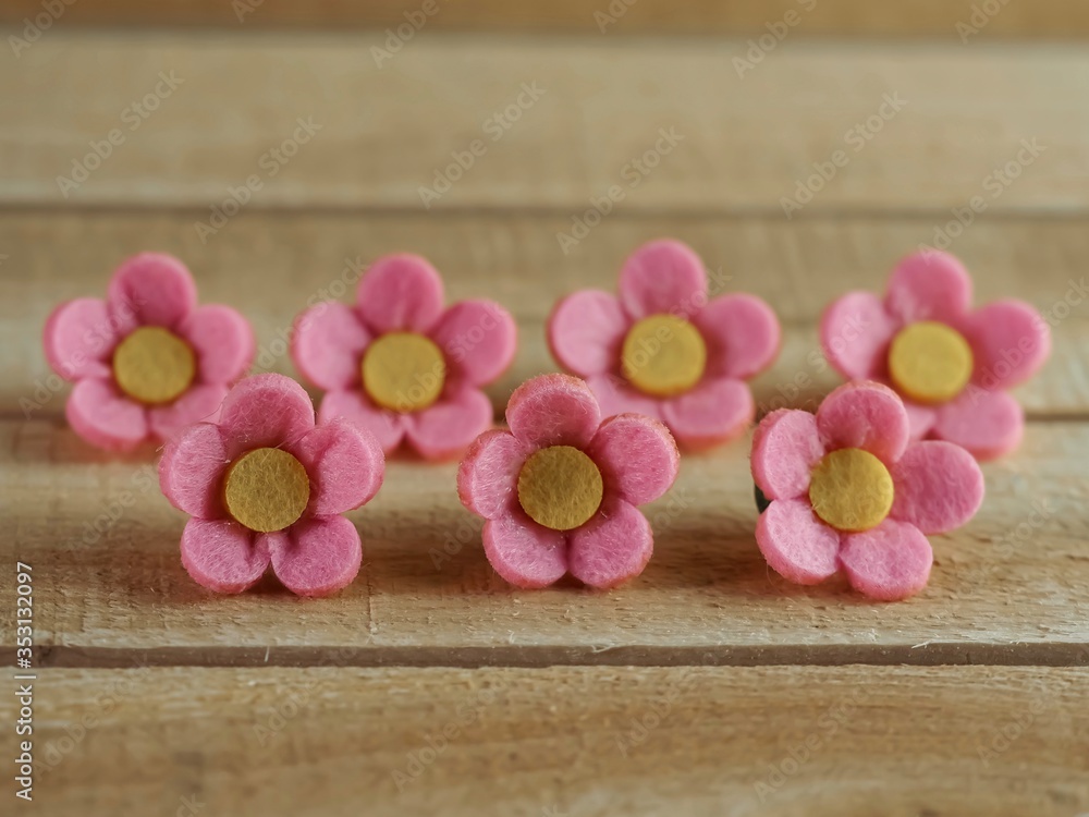 7 pink felt flowers with yellow centers lined up on a piece of real wood. Perfect for crafts or accessories. 7 pink felt flowers with yellow centers lined up on a piece of real wood. Perfect for crafts or accessories.