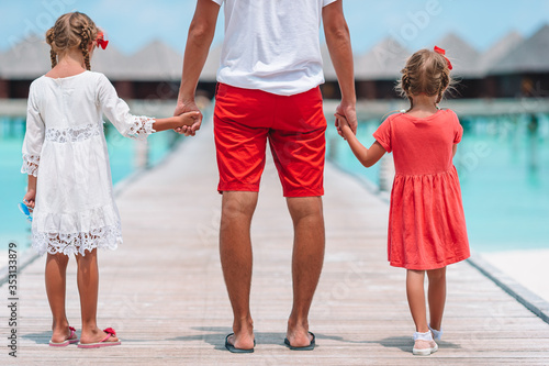Little girls with dad on wooden jetty near water bungalow at exotic resort