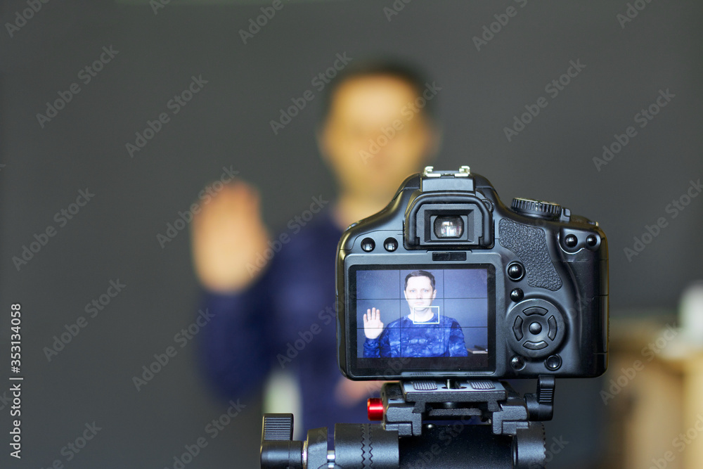 A blogger takes himself on camera. In focus is his camera and the image on it. Gesture of greeting. Everything else is blurry.
