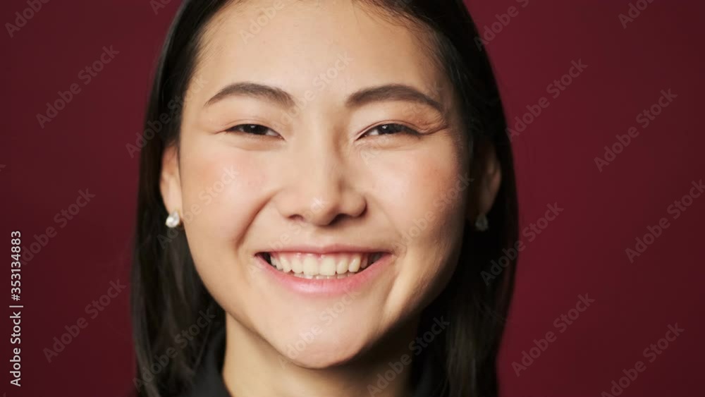 A close-up view a charming asian woman is smiling standing isolated over red background A close-up view a charming asian woman is smiling standing isolated over red background