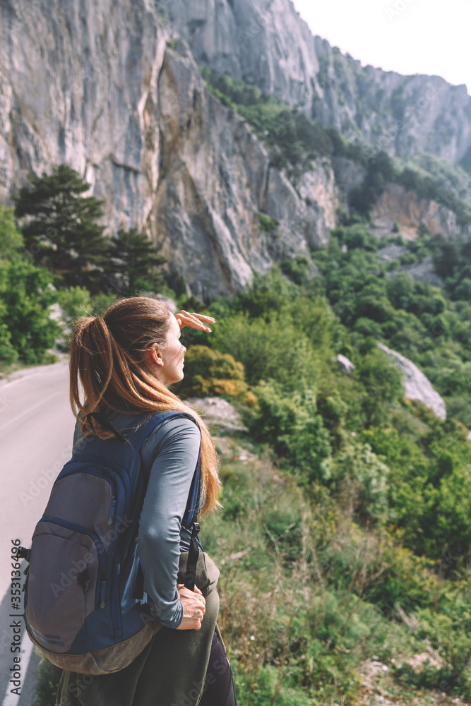 Naklejka premium Traveling woman sitting near mountain and looking far away Spring weather, calm scene. Hiking outdoors, landscape view in the sunlight. A series of photos of Wanderlust.