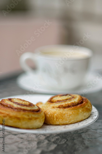 Outdoor breakfast. Freshly baked cinnamon buns and cup of coffee on a glass table. 