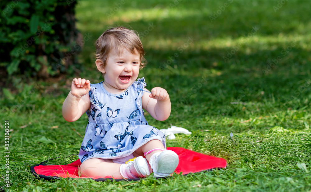 Happy Cute Baby Girl Sitting in the Summer Park and Laughing Happy Cute Baby Girl Sitting in the Summer Park and Laughing