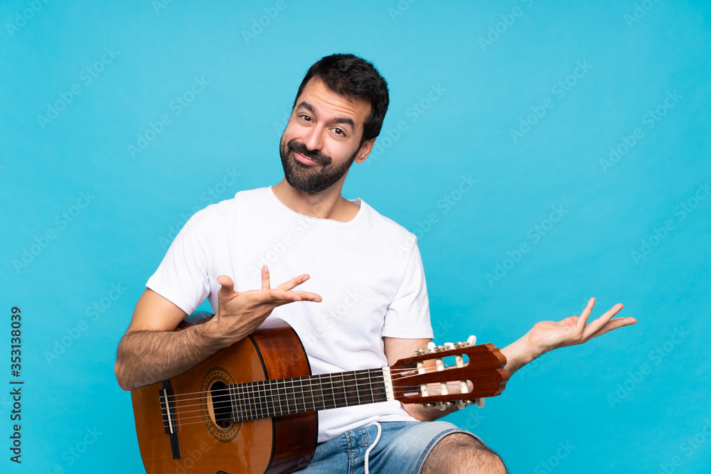 Obraz premium Young man with guitar over isolated blue background extending hands to the side for inviting to come
