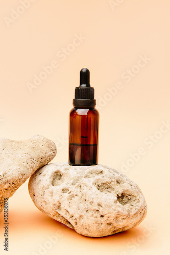 Beautiful composition with tea oil. Glass cosmetic bottles stand on a stone on a beige background with bright sunlight. Natural cosmetics concept, natural essential oil