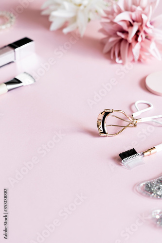 Cosmetic products: lip gloss, lipstick, jade roller, brushes, patches and eyelash curler on pink background. Beauty and makeup concept. 