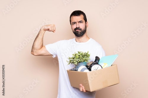 Man holding a box and moving in new home over isolated background doing strong gesture