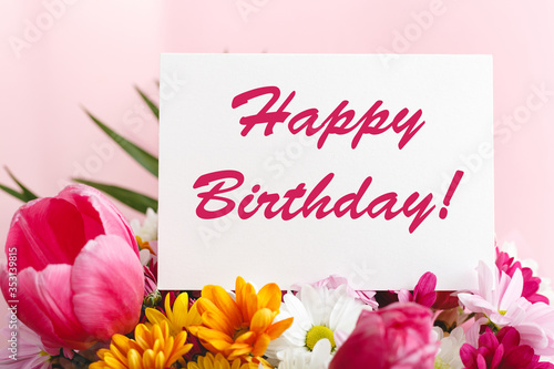 Happy birthday text on card in flower bouquet on pink background. Greeting card in Tulips, daisies, chrysanthemum beautiful spring bouquet. Flower delivery, congratulation card.