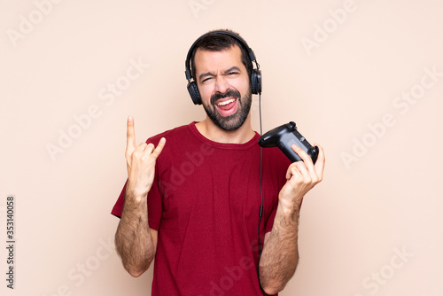 Man playing with a video game controller over isolated wall making rock gesture