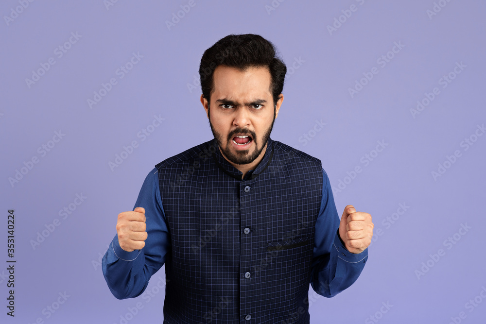 Millennial Indian man clenching his fists in anger against color background Millennial Indian man clenching his fists in anger against color background