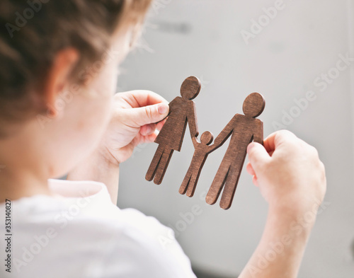 The little child looking on the wooden figures of mom, dad and child in his hands. Concept of the child dreaming about family