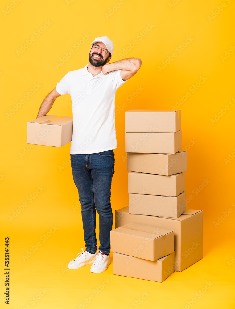 Full-length shot of delivery man among boxes over isolated yellow background with neckache Full-length shot of delivery man among boxes over isolated yellow background with neckache
