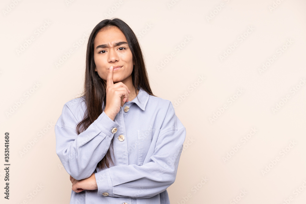 Young Indian woman isolated on beige background having doubts while looking up Young Indian woman isolated on beige background having doubts while looking up
