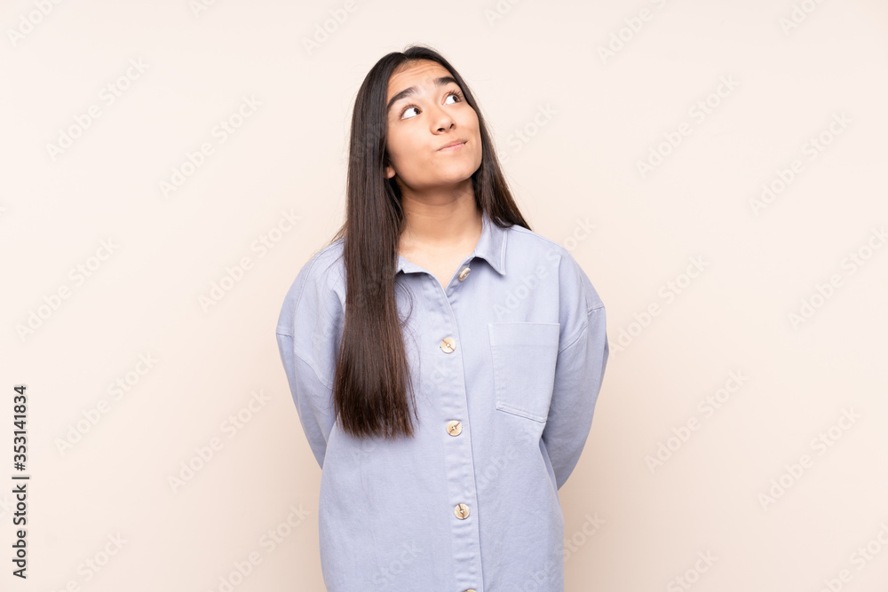 Young Indian woman isolated on beige background and looking up Young Indian woman isolated on beige background and looking up