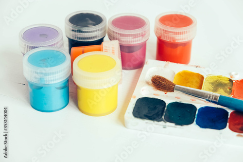 Colorful gouache paints and brush for painting on white wooden table. Copy, empty space for text