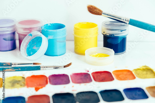 Colorful gouache paints and brushes for painting on white wooden table. Copy, empty space for text
