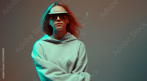 Foto Portrait of a stylish young girl, cool posing in a hoodie, sunglasses and with developing hair, on a neon background