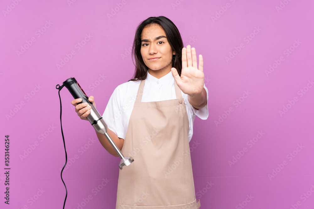 Indian woman using hand blender isolated on purple background making stop gesture with her hand Indian woman using hand blender isolated on purple background making stop gesture with her hand