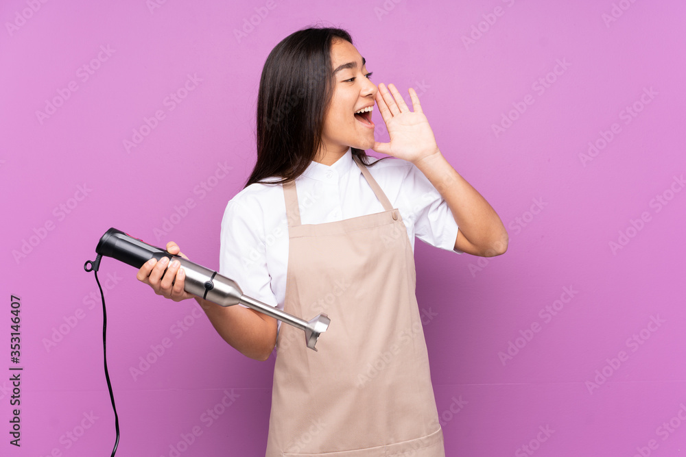 Indian woman using hand blender isolated on purple background shouting with mouth wide open Indian woman using hand blender isolated on purple background shouting with mouth wide open