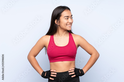 Young Indian sport woman isolated on blue background posing with arms at hip and looking side