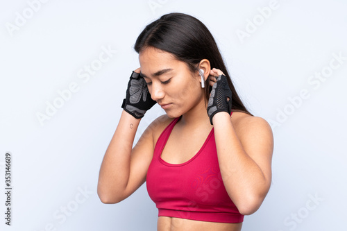 Young Indian sport woman isolated on blue background listening music © luismolinero
