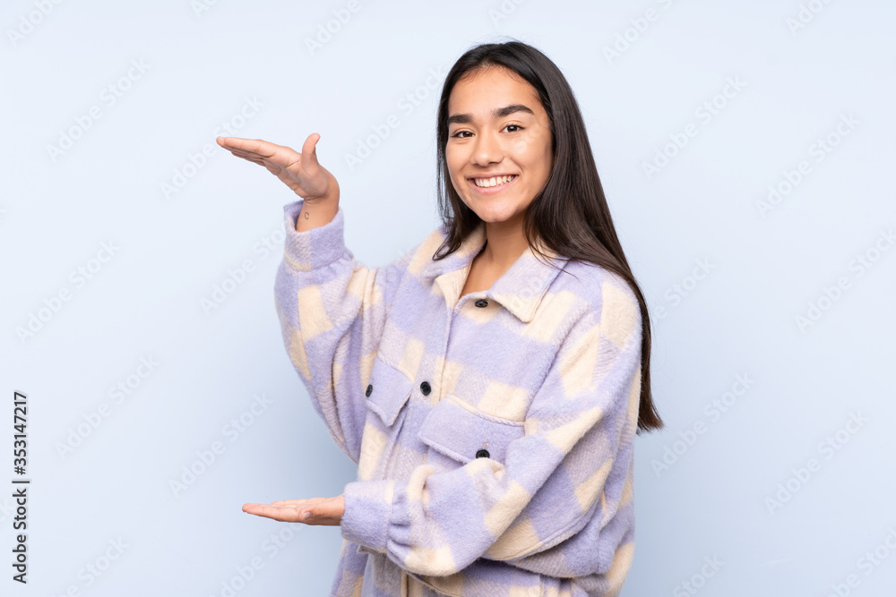 Young Indian woman isolated on blue background holding copyspace to insert an ad Young Indian woman isolated on blue background holding copyspace to insert an ad