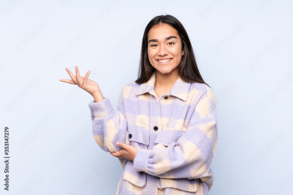 Young Indian woman isolated on blue background extending hands to the side for inviting to come Young Indian woman isolated on blue background extending hands to the side for inviting to come